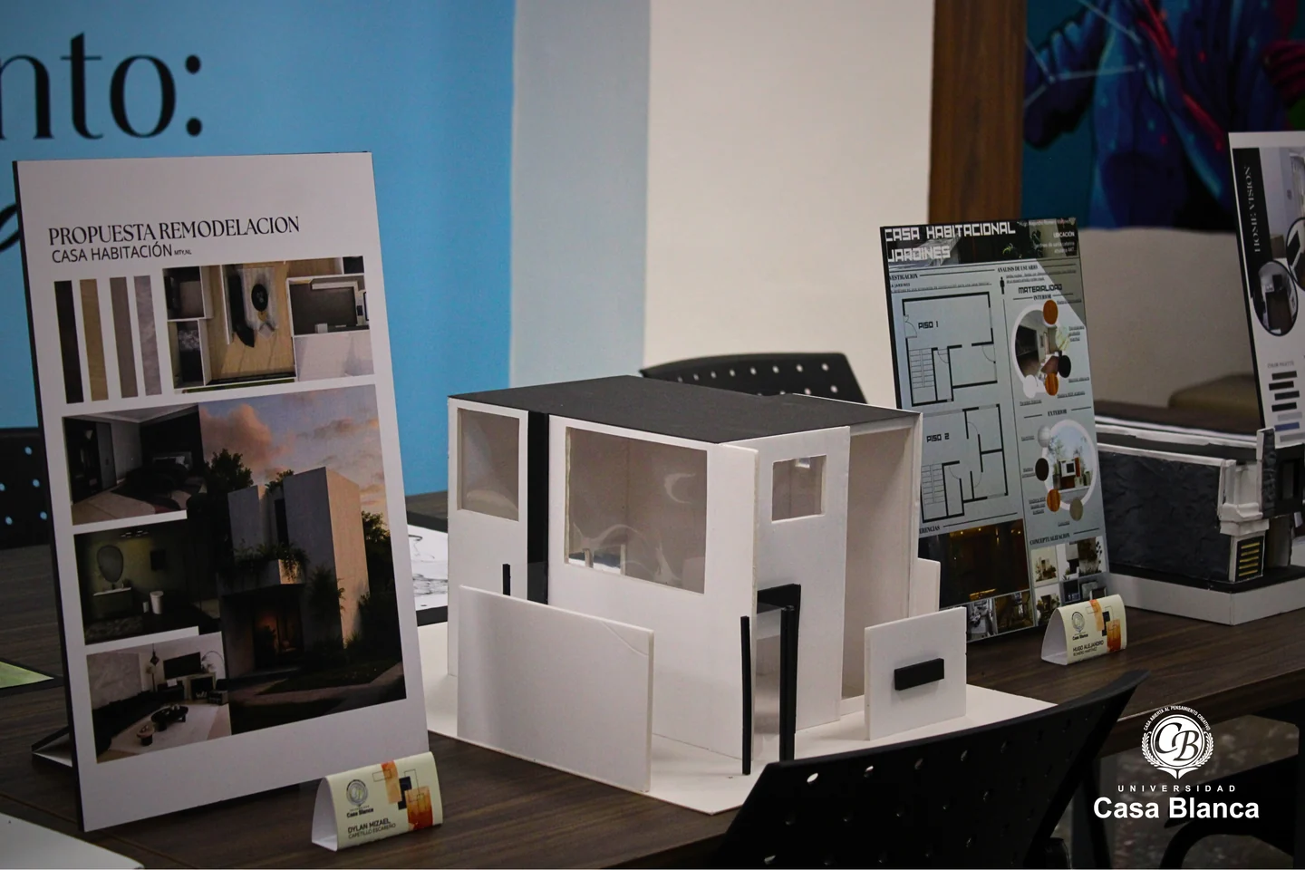 Maquetas de edificios acompañadas por láminas de planos en una exhibición