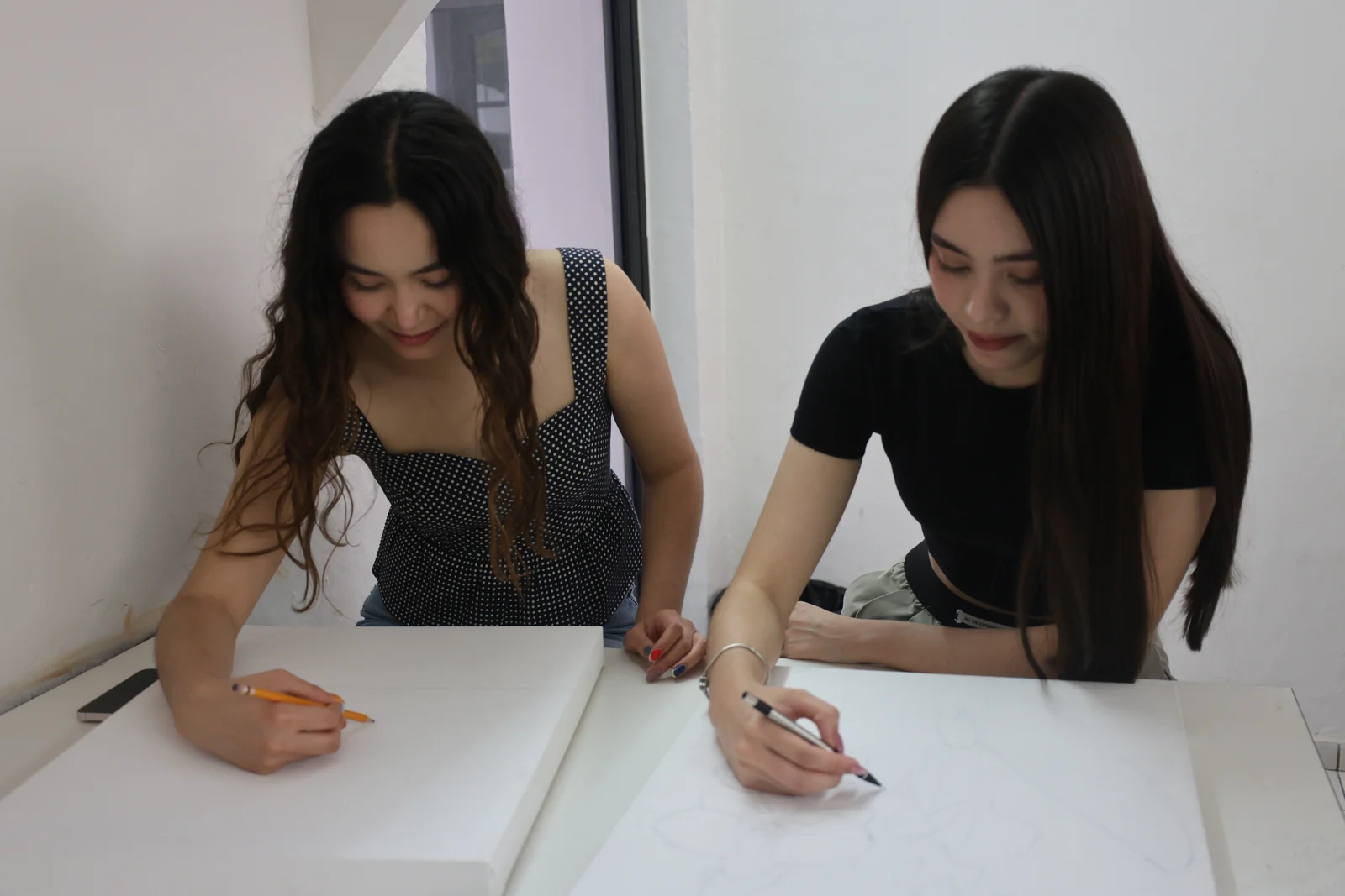 Dos estudiantes dibujan sobre papel en una mesa del aula