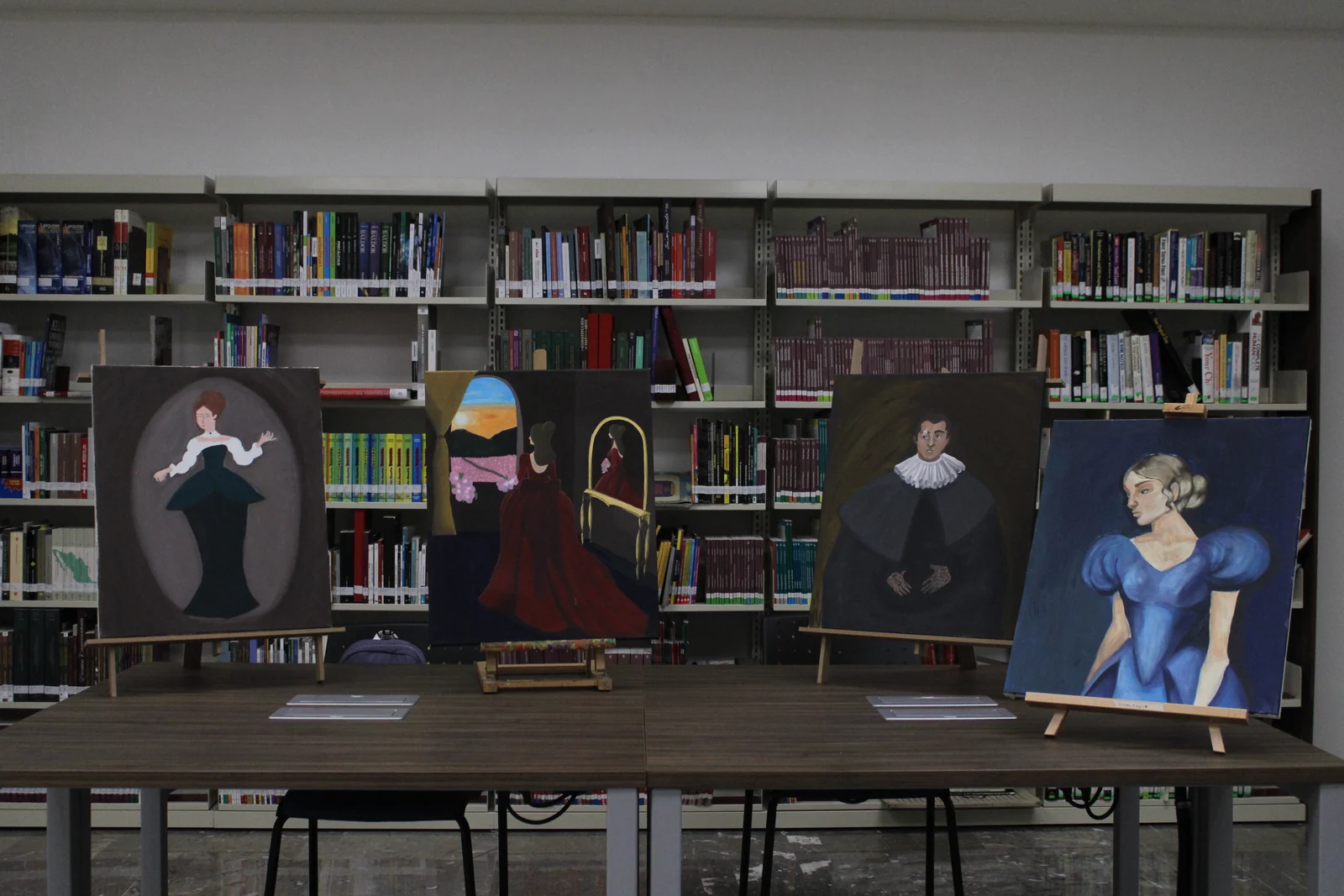 Piezas gráficas y retratos expuestos frente a los estantes de la biblioteca