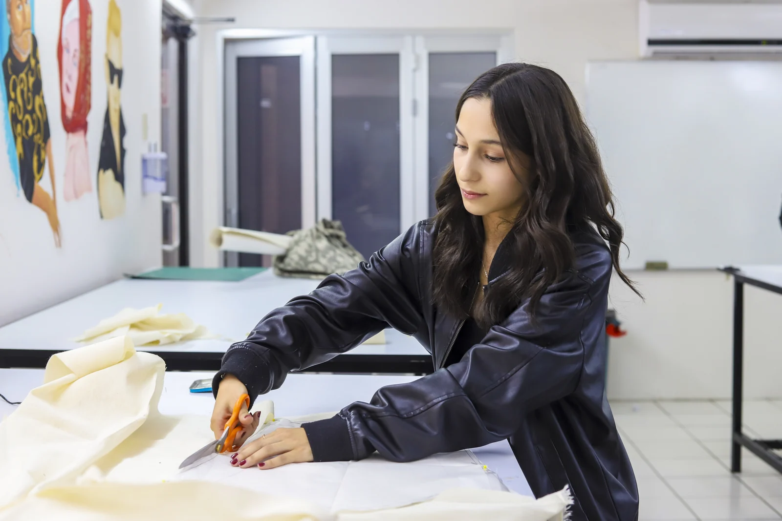 Estudiante trabaja con tela y herramientas de corte en una mesa del taller